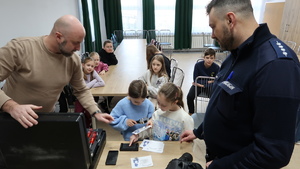 Dzieci robią odbitki swoich linii papilarnych. Obok stoi policjant i technik kryminalistyki.