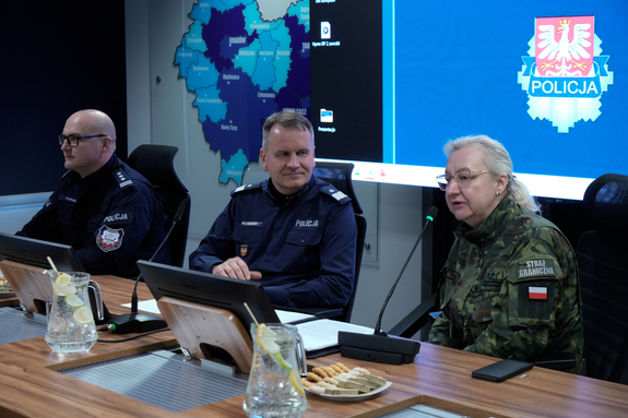 Dwóch policjantów i przedstawicielka straży granicznej siedzą przy stole.