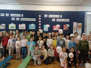 Policjant stoi razem z dziećmi na tle gazetki szkolnej o tematyce akcji No promil No problem.