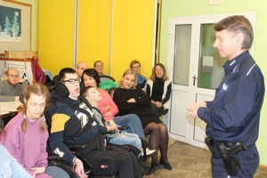 Policjant stojąc prowadzi prelekcje do podopiecznych domu opiekuńczo-rehabilitacyjnego.