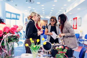 Kilka pań rozmawia z makijażystką nad stołem z przyborami do makijażu.