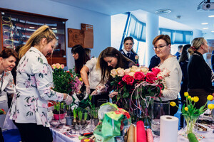 Panie przy stole tworzą kompozycje florystyczne.