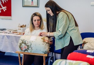 Instruktorka pokazuje innej pani jak wykonuje się koronkę klockową.