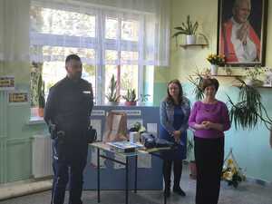 Policjant i dwie nauczycielki obok stołu na którym leżą nagrody w konkursie.