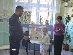 Policjant wręcza nagrodę jednej z uczestniczek konkursu. Obok stoi nauczycielka.
