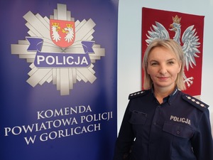 Policjantka obok baneru reklamowego z policyjna gwiazda i napisem komenda powiatowa policji w Gorlicach.