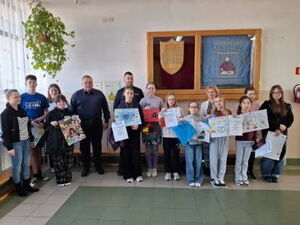 Policjant nauczyciel i uczniowie stoją ze swoimi pracami plastycznymi.