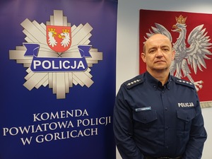 Policjant stoi obok baneru reklamowego z gwiazda policyjną i napisem Komenda Powiatowa Policji w Gorlicach.