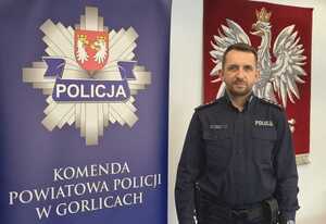 Policjant stoi obok baneru reklamowego z gwiazdą policji i napisem Komenda Powiatowa Policji w Gorlicach.