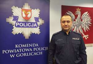 Policjant stoi przy banerze reklamowym z policyjną gwiazdą i napisem Komenda Powiatowa Policji w Gorlicach.