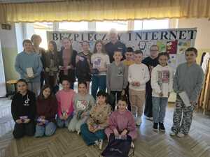 Dzieci stoją razem z policjantem na tle gazetki z napisem Bezpieczny Internet, na której są prace plastyczne uczniów.