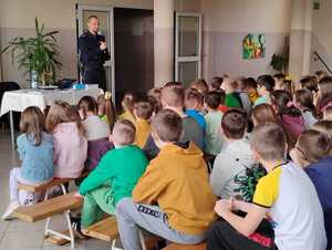 Uczniowie siedząc słuchają prelekcji policjanta.