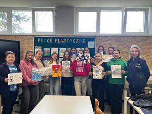 Policjantka razem z uczniami stojącymi i prezentującymi swoje prace plastyczne.