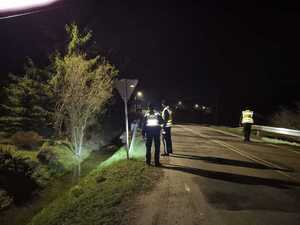 Trzech policjantów idąc drogą przeszukuje przy pomocy latarek przydrożne rowy.