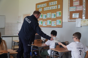 Policjant podaje kartkę z testem wiedzy uczniowi siedzącemu w ławce.