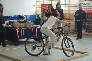 Uczennica pokonuje jedna z przeszkód na rowerze, na sali, obok stoi policjant.