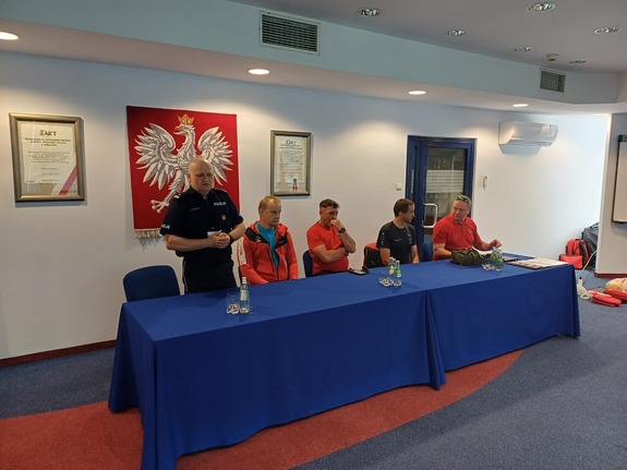 Policjant i kilku przedstawicieli GOPR przy stole.