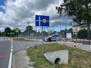 W pobliżu szkoły przy drodze stoi policjant przy radiowozie.