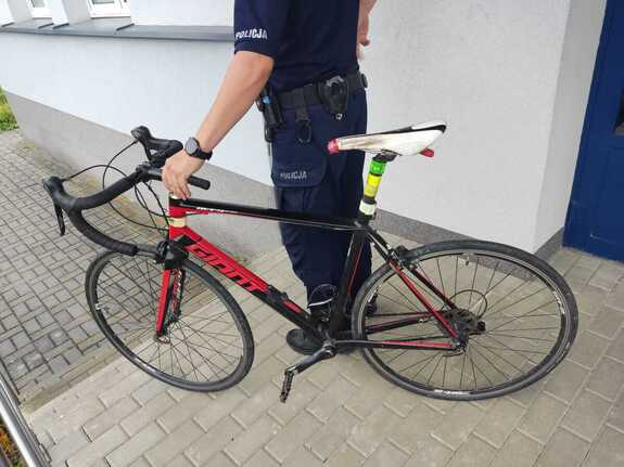 Policjant stojąc trzyma odzyskany rower koloru czarno-czerwonego.
