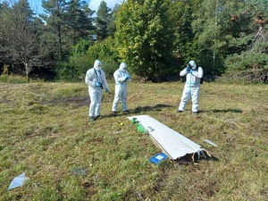 Trzech ubranych w białe kombinezony policjantów robi zdjęcia na miejscu wypadku.