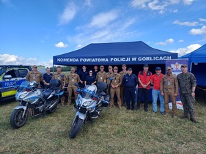 Przy stoisku Policji stoją policjanci, żołnierze i goprowcy.