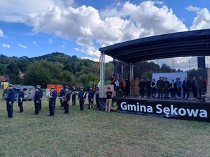 Na scenie stoją zaproszeni goście. O bok sceny stoi orkiestra policyjna.