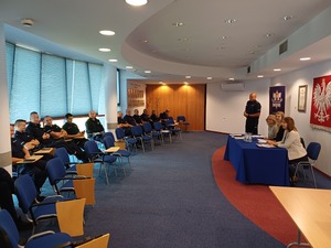 Na auli przy stole siedzą trzy kobiety, na przeciw na krzesłach siedzą policjanci.