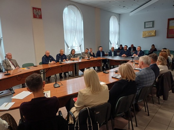 Dwóch policjantów razem z kilkunastoma osobami siedzą przy dużym stole.