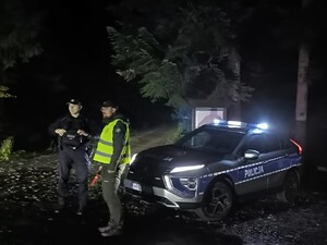 Przy radiowozie po zmroku stoi policjant i strażnik leśny.