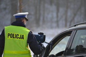 Policjant stoi tyłem obok samochodu i pokazuje kierowcy zapis ujawnionego wykroczenia na mierniku prędkości.