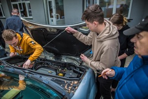 Obok samochodu z otwartą pokrywą silnika stoi instruktor i dwóch uczestników turnieju, którzy sprawdzają czy pojazd jest sprawny i gotowy do jazdy.