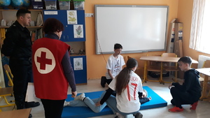 Na materacu leży osoba poszkodowana w wypadku. Trzy osoby udzielają jej pierwszej pomocy. Instruktorzy ze straży pożarnej i PCK obserwują wykonywanie zadania.