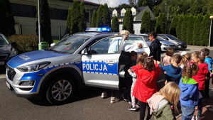 Przedszkolaki stoją przed radiowozem policyjnym, niektóre wsiadają do pojazdu.