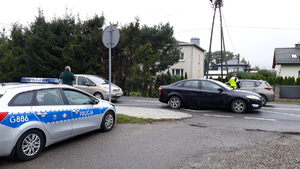 Policjant sprawdza trzeźwość kierujących, którzy jadą samochodami  drogą. Obok na poboczu stoi policyjny radiowóz.