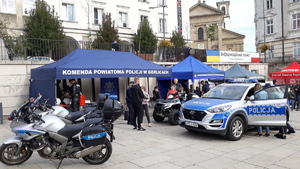 Na płycie rynku stoi namiot Komendy Powiatowej Policji w Gorlicach, a przed namiotem stoi policyjny quad, radiowóz i dwa motocykle. Rodziny z dziećmi oglądają policyjny sprzęt. W tle inne namioty.