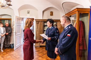 Komendant Powiatowy Policji w Gorlicach wraz ze swoim zastępcą wręczają list gratulacyjny jednej z pracownic.