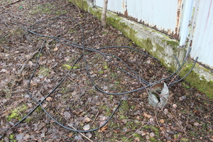 Rozciągnięte kable elektryczne leżące na ziemi przy ogrodzeniu.