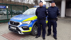 Dwóch policjantów stoi przy radiowozie.