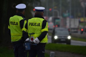 Dwóch policjantów stoi przy drodze i obserwuje ruch pojazdów.