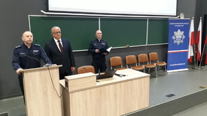 Komendant Powiatowy Policji w Gorlicach wraz z Przewodniczącym Rady Powiatu otwierają konferencję. Obok stoi policjant -moderator konferencji.