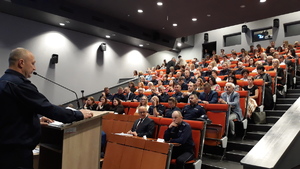 Uczestnicy konferencji siedzą i słuchają moderatora konferencji.