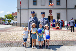 Na płycie rynku w Bieczu stoi dwóch policjantów z trójką dzieci. W tle budynek Urzędu  Miasta.