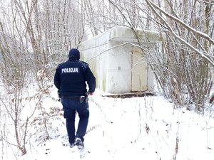 Policjant idzie skontrolować samotnie stojący w lesie barak mieszkalny zasypany śniegiem.