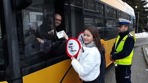 Dwie młode osoby podają ulotki informacyjne kierowcy autobusu, obok stoi policjant.