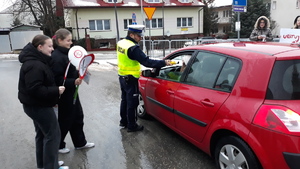 Policjant sprawdza trzeźwość kierującego, obok stoją dwie młode osoby aby podać ulotki kierowcy