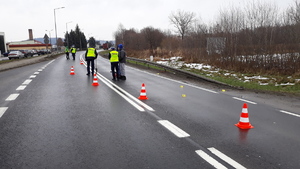 Kilku policjantów stoi na ulicy, obok stoją pachołki drogowe wyznaczające miejsce wypadku.