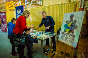 Policjant daje ulotki informacyjne i odblaski dzieciom, które stoją przy stoisku profilaktycznym policji