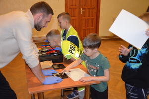 Jedno z dzieci wykonuje odbitkę swoich linii papilarnych pod nadzorem technika kryminalistyki.